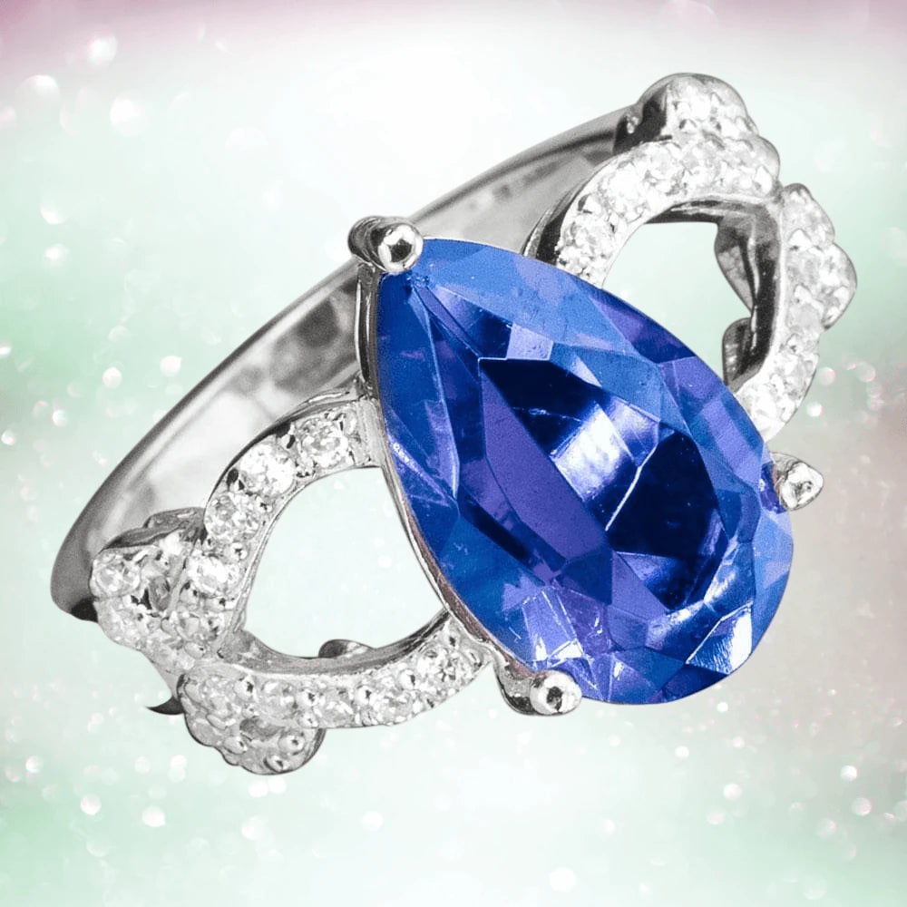 Essence Ring featuring a large pear-shaped blue gemstone set in sterling silver with intricate detailing and small clear stones, designed for women’s jewelry collections.