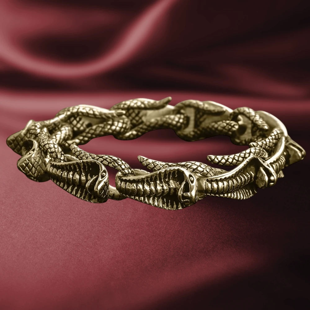 Venom Men's Gold Bracelet made from stainless steel with a gold plating, featuring an intricate design of connected serpent heads, displayed on a rich burgundy fabric background.