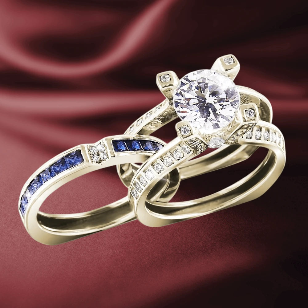Natalia Gold Ring featuring a large round center stone set in gold-plated sterling silver, accompanied by two complementary rings with blue and clear stones on a rich burgundy background.