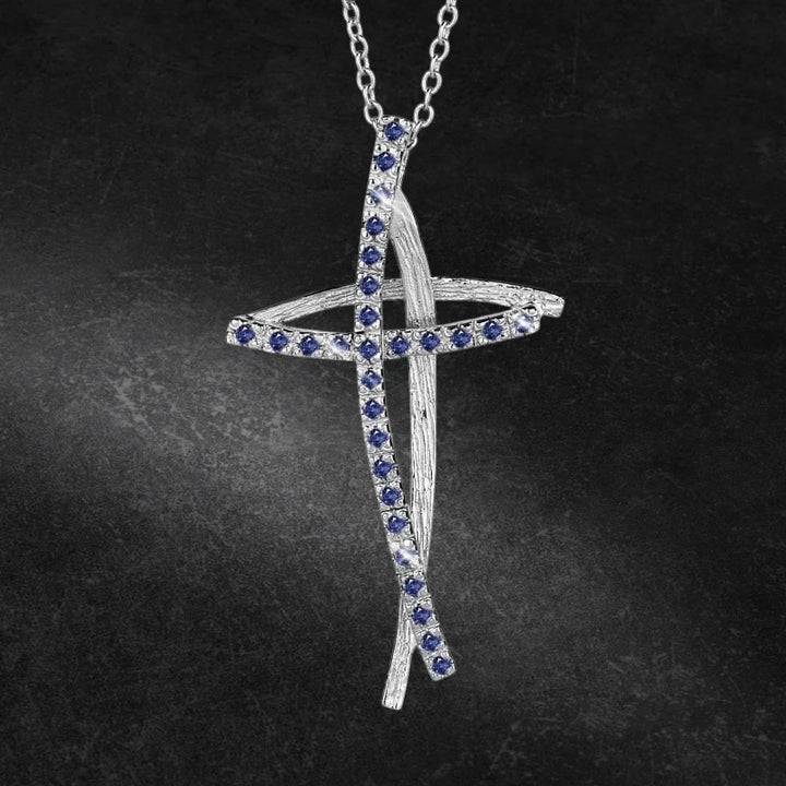 Decoria Rhodium Cross Pendant featuring a delicate rhodium plating with blue gemstone accents on a feminine chain necklace against a dark background.