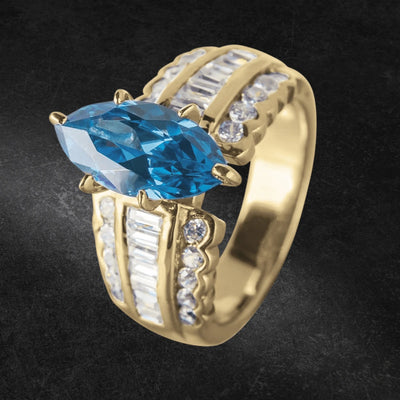 Carman Marquise Ring featuring a gold-plated stainless steel band adorned with clear baguette and round stones, highlighted by a striking blue marquise-cut centerpiece.