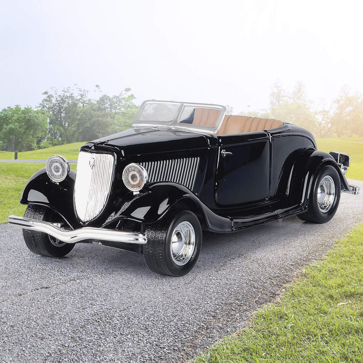 Black vintage convertible car with a glossy finish parked on a gravel driveway beside a green lawn and trees