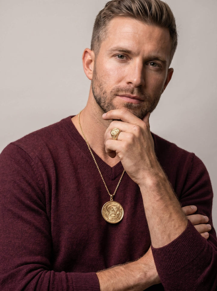 Man wearing a gold American Glory Ring and matching gold pendant necklace dressed in a burgundy sweater against a neutral background