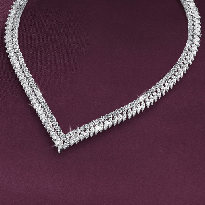 Sparkling necklace with layered rows of clear stones and repeating leaf-shaped details arranged in a V curve against a deep plum background