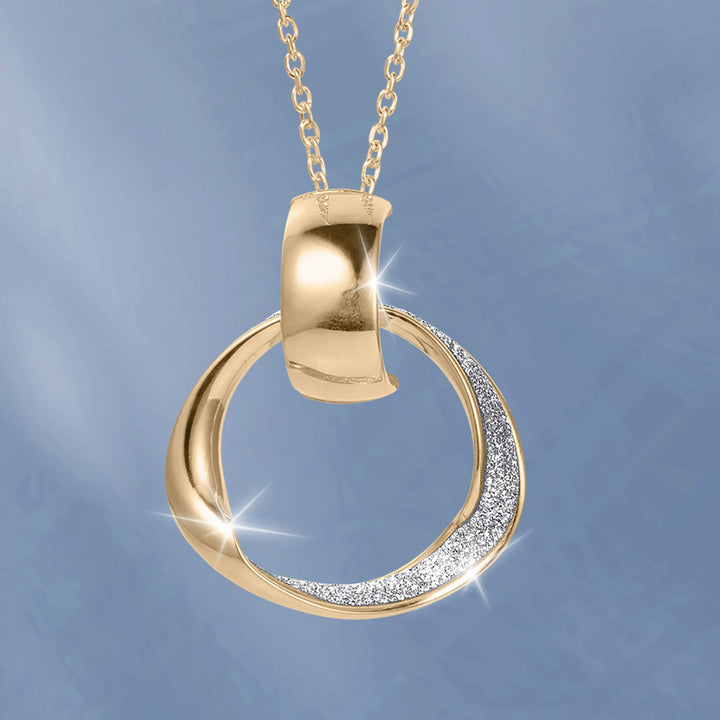 Gold circular pendant necklace with a polished curved bail and sparkling stone accents against a soft blue background