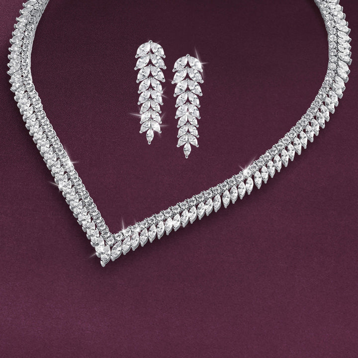 Sparkling silver tone necklace and matching dangling earrings arranged on a deep burgundy background with layered leaf shaped stone details