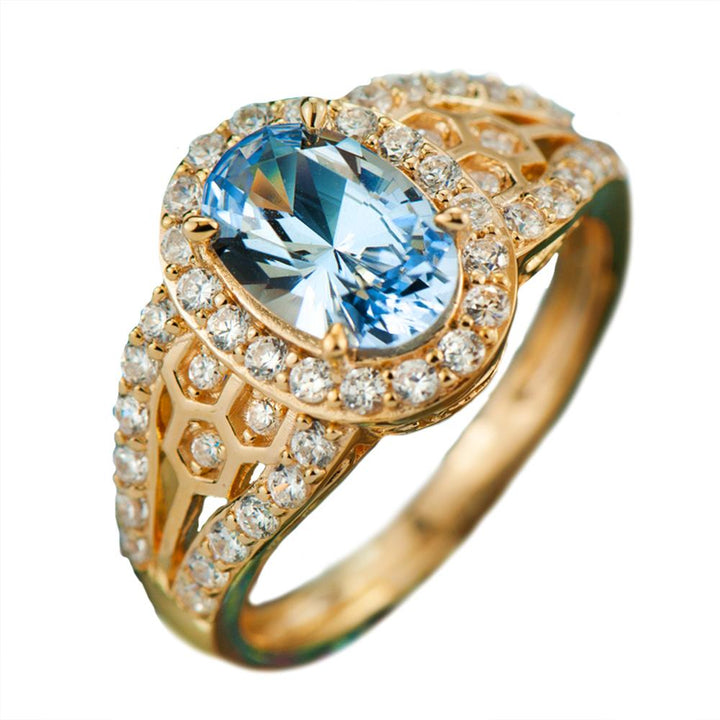 Sky Honeycomb Ring featuring a sterling silver base plated in gold, adorned with a large oval blue gemstone center and surrounded by smaller clear stones, designed for women.